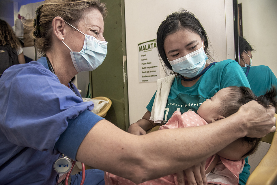 Two members of staff in surgical gowns and face masks caring for a patient.