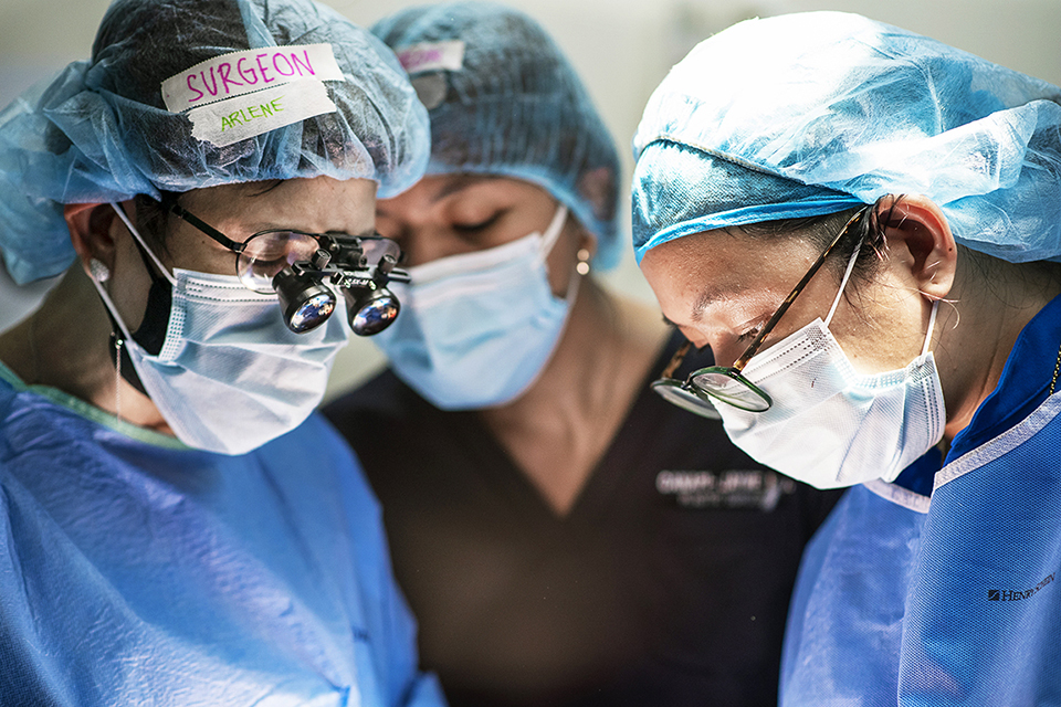Three members of surgical staff wearing surgical cap, gown and face masks, look down.