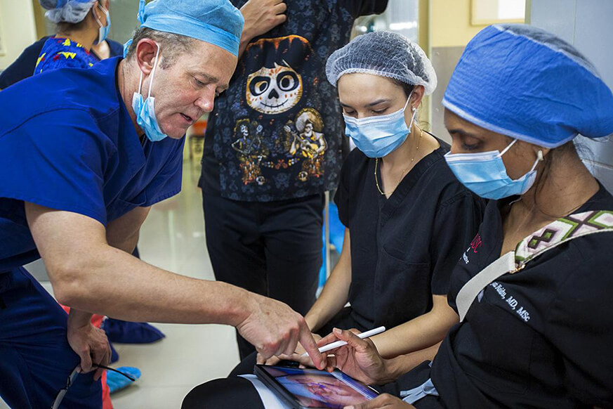 Surgeons sat in a hospital hallway, looking at images on an iPad and discussing surgery. 