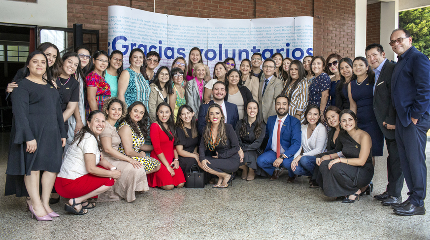 A group of 42 staff and volunteers pose for a photo in front of a banner that says 'gracias voluntarios' (thank you volunteers)