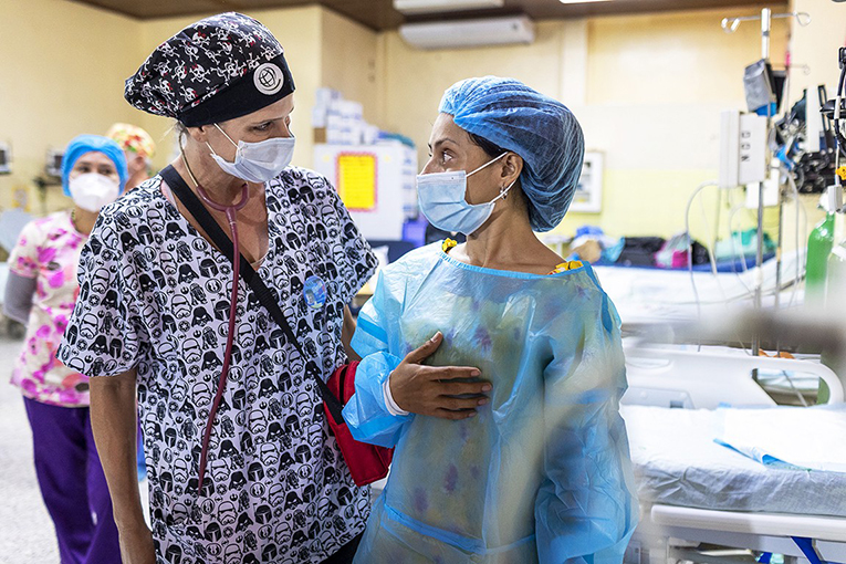 Zoe's mum Ana talking to volunteer Ana Luisa in the post operative ward. Both are wearing surgical gowns, hats and masks.