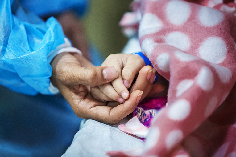 Ana holds Zoe's hand, which is under a pink spotted blanket.