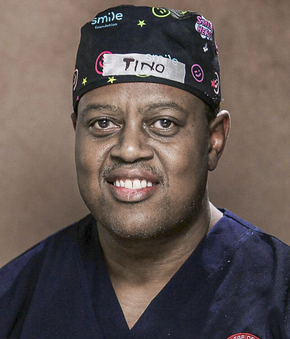 A smiling man in dark blue medical scrubs and a colorful surgical cap labeled "Tino" faces the camera. A circular embroidered patch with "College of Surgeons" is visible on his scrubs.